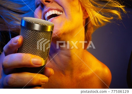 Female vocalist under gelled lighting sings with passion into condenser microphone. 77586129