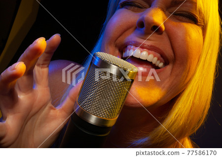 Female vocalist under gelled lighting sings with passion into condenser microphone. Female vocalist under gelled lighting sings with passion into condenser microphone. 77586170