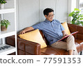 senior asian man reading book on sofa 77591353
