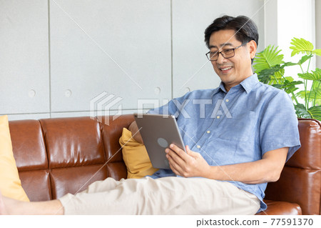 senior asian man using digital tablet on sofa senior asian man using digital tablet on sofa 77591370