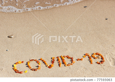 Inscription Covid-19 made of amber stones and incoming sea wave on sand at beach. Safe holidays 77593063