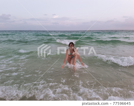 A young woman in a swimsuit runs into the sea on the waves and laughs. A young woman in a swimsuit runs into the sea on the waves and laughs. 77596645