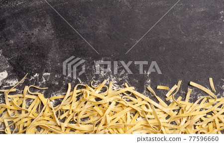 Fresh pasta background. Homemade Italian fettuccine pasta cooked in the home kitchen with fresh eggs and flour on a wooden background. Italian food and cuisine concept Fresh pasta background. Homemade Italian fettuccine pasta cooked in the home kitchen with fresh eggs and flour on a wooden background. Italian food and cuisine concept 77596660