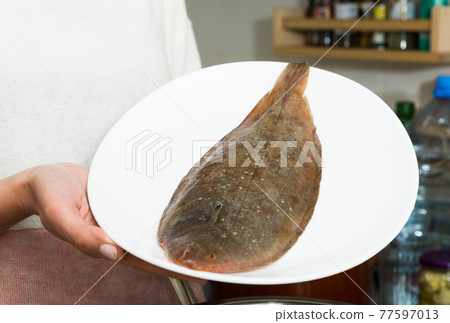 Fresh black sole on plate in hands of woman 77597013