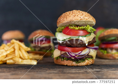 Double Hamburger with tomatoes, onions, cucumber, lettuce , melting cheese and french fries  served on a  rustic wooden table 77597251