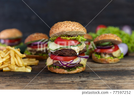 Double Hamburger with tomatoes, onions, cucumber, lettuce , melting cheese and french fries  served on a  rustic wooden table 77597252