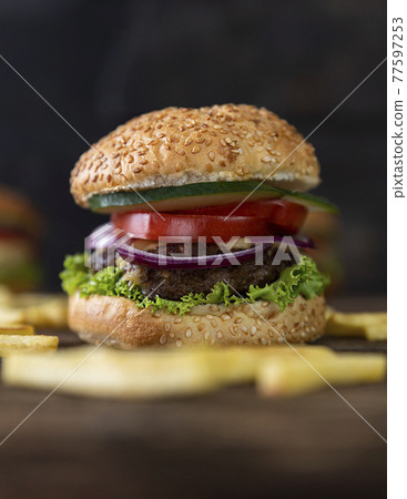 Hamburger with tomatoes, onions, cucumber, lettuce , melting cheese and french fries served on a  rustic wooden table 77597253