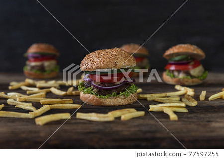 Hamburgers with tomatoes, onions, cucumber, lettuce , melting cheese and french fries served on a rustic wooden table Hamburgers with tomatoes, onions, cucumber, lettuce , melting cheese and french fries served on a rustic wooden table 77597255