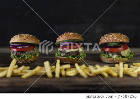 Hamburgers with tomatoes, onions, cucumber, lettuce , melting cheese and french fries served on a  rustic wooden table 77597256