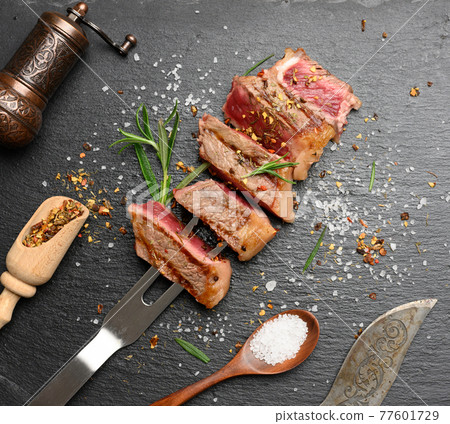 sliced fried beef steak New York  striploin on a black background with spices, degree of doneness rare 77601729