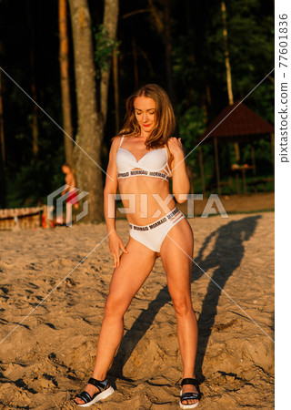 Caucasian fit woman with sport body is posing on beach at sunset time. 77601836