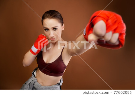 A blow with bandaged fists into the camera. Studio portrait of attractive Caucasian young female fighter with bandages on her fists preparing for battle and looking at the camera. A blow with bandaged fists into the camera. Studio portrait of attractive Caucasian young female fighter with bandages on her fists preparing for battle and looking at the camera. 77602095