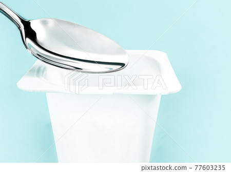 Yogurt cup and silver spoon on mint background, white plastic container with yoghurt cream, fresh dairy product for healthy diet and nutrition balance 77603235