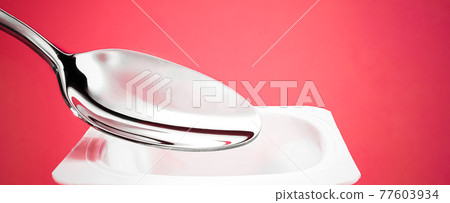 Yogurt cup and silver spoon on red background, white plastic container with yoghurt cream, fresh dairy product for healthy diet and nutrition balance 77603934