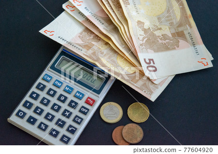 Calculator with 50 euro banknotes and coins on a gray-black background. Close -up 77604920