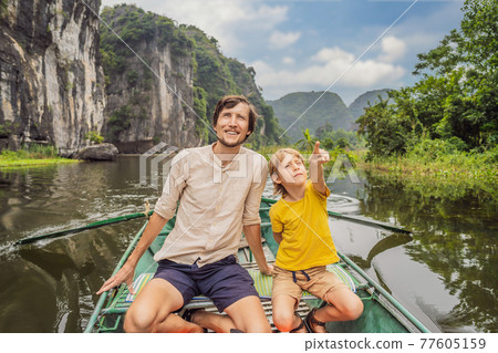 Dad and son tourists in boat on the lake Tam Coc, Ninh Binh, Viet nam. It's is UNESCO World Heritage Site, renowned for its boat cave tours. It's Halong Bay on land of Vietnam. Vietnam reopens borders 77605159