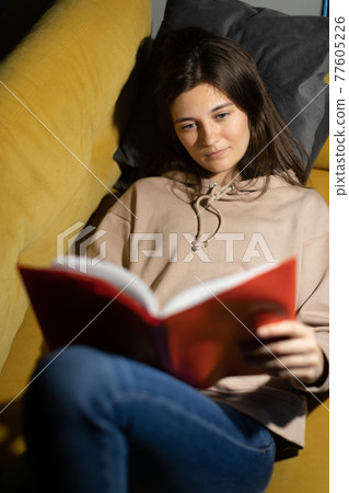 Attractive long-haired girl reads book alone at home lying on comfy sofa 77605226