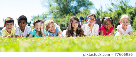 Happy children lie on the green grass on a sunny day Happy children lie on the green grass on a sunny day 77606986