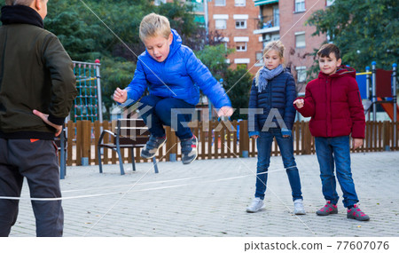Children jump through an elastic rope in a children playground Children jump through an elastic rope in a children playground 77607076