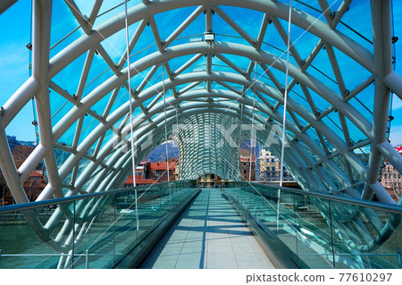 Modern stylish design made of glass and metal, pedestrian bridge over the Kura river in Tbilisi Modern stylish design made of glass and metal, pedestrian bridge over the Kura river in Tbilisi 77610297
