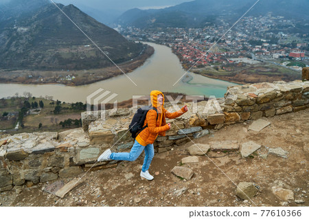 Young girl tourist rejoices posing against the backdrop of an amazing natural landscape. The confluence of two rivers in the city of Mtskheta in Georgia 77610366
