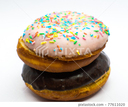 Chocolate doughnut over a doughnut with powdered sugar colored on a white background. Close-up and floating focus 77611020
