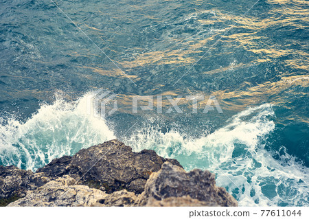Splashes from the waves bumping against the rocky shore 77611044