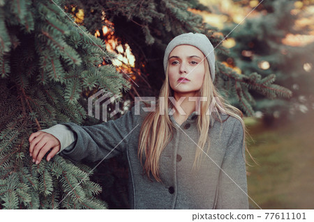 blond girl in knitted hat and coat close up portrait on on blue spruce background blond girl in knitted hat and coat close up portrait on on blue spruce background 77611101