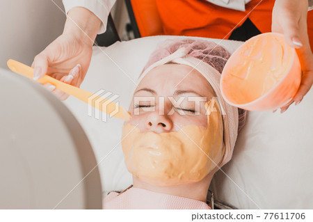 Woman at the beautician applying a relaxing golden mask on the face, restoring and moisturizing the skin. 77611706