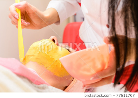 Applying a gold mask on a woman's face, a procedure in a beauty salon. 77611707