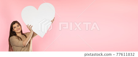 Girl with a large white heart shape in the hands. A student in love stands and holds a large heart shape in her hands. Valentine's Day and love. Panoramic frame. Girl with a large white heart shape in the hands. A student in love stands and holds a large heart shape in her hands. Valentine's Day and love. Panoramic frame. 77611832