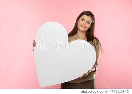 Girl with a large white heart shape in the hands. A student in love stands and holds a large heart shape in her hands. Valentine's Day and love. 77611845