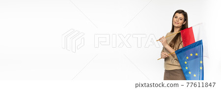 Young girl with the flag of the European Union and Poland. The student is holding two flags in her hand. Woman with flags on white background. Panoramic frame. Young girl with the flag of the European Union and Poland. The student is holding two flags in her hand. Woman with flags on white background. Panoramic frame. 77611847