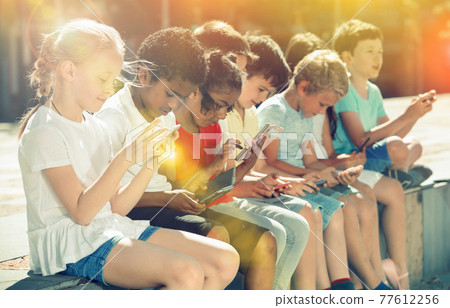 Positive kids sitting at urban street with mobile devices Positive kids sitting at urban street with mobile devices 77612256
