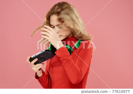Woman with mobile set-top box headphones playing lifestyle pink background red jacket Woman with mobile set-top box headphones playing lifestyle pink background red jacket 77618977