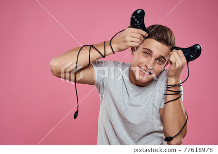 A man holds over his head joysticks wires on his hands entertainment leisure lifestyle games pink background A man holds over his head joysticks wires on his hands entertainment leisure lifestyle games pink background 77618978