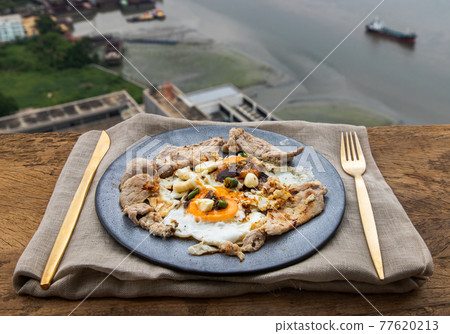 Breakfast with Fried egg, Roasted pork sprinkle garlic, chili in plate with Knife and fork on old wooden table. 77620213