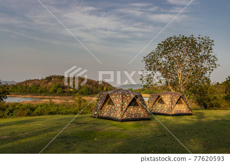 View of two camping tent with awning pitched on the dry ground Near beautiful big trees with branches at the campsite in lake shore with mountain range in background. 77620593