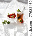 Cup of tea and wild strawberries on a white lace background 77622460