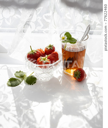 Cup of tea and wild strawberries on a white lace background 77622460