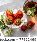 Cup of tea and wild strawberries on a white lace background 77622469