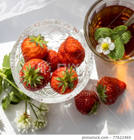 Cup of tea and wild strawberries on a white lace background 77622469