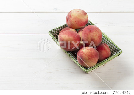 Fresh, ripe peaches in a basket on a white wooden background. Fresh, ripe peaches in a basket on a white wooden background. 77624742