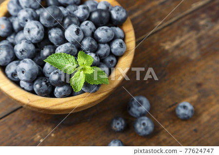 Freshly picked blueberries in wooden bowl on wooden background.  77624747
