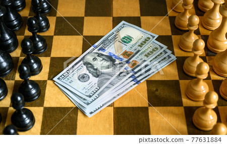 Dollar bills between chess pieces rows on chessboard 77631884