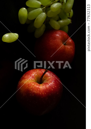 Two ripe fresh red apples with water drops on glossy peel and bunch of green grapes on black background Two ripe fresh red apples with water drops on glossy peel and bunch of green grapes on black background 77632313