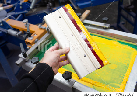 Squeegee for Serigraphy silk screen print process in hand at clothes factory. Frame, squeegee and plastisol color paints Squeegee for Serigraphy silk screen print process in hand at clothes factory. Frame, squeegee and plastisol color paints 77633168