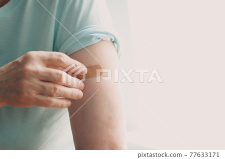 Vaccination elderly woman in doctor office with adhesive covid-19 vaccine plaster. 77633171