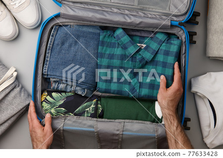 Man packing travel suitcase with clothes 77633428