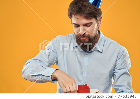 Man with cake on yellow background birthday party hat cropped view 77633945
